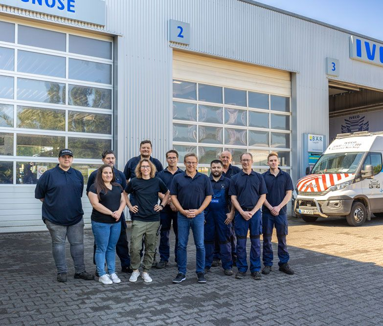 Ein Arbeiter mit blauen Handschuhen montiert in einer Fabrikwerkstatt ein Fahrzeugchassis.