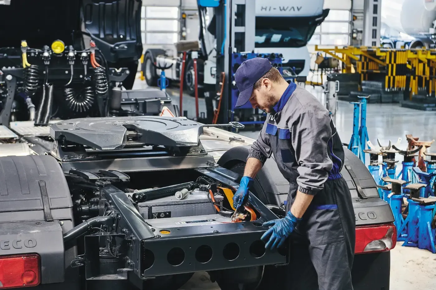 Ein Arbeiter mit blauen Handschuhen montiert in einer Fabrikwerkstatt ein Fahrzeugchassis.