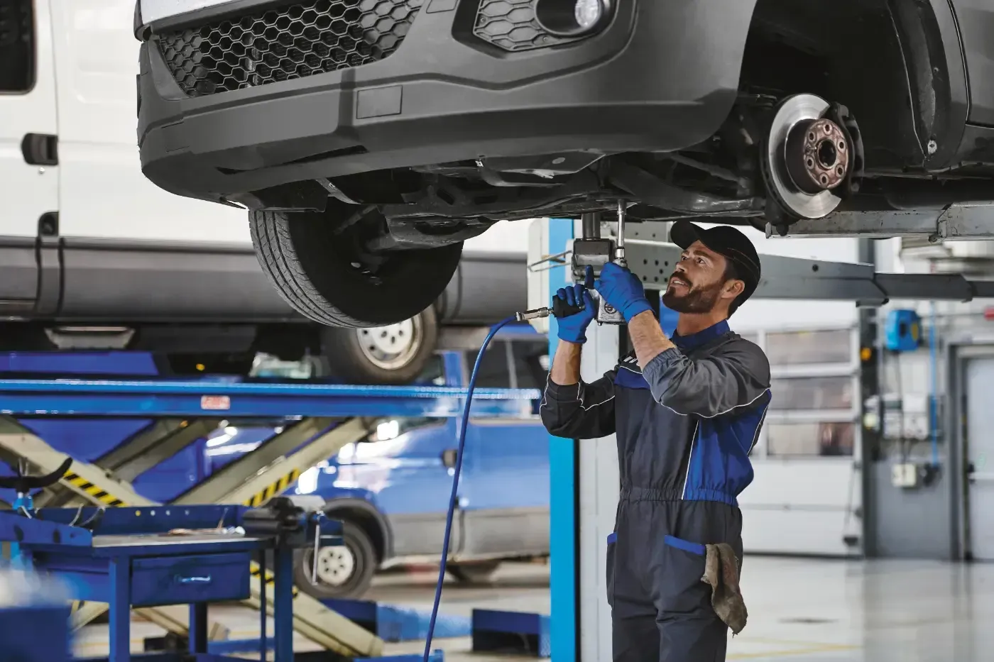 Ein Mechaniker untersucht ein Auto auf einer Hebebühne in einer Autowerkstatt und benutzt dabei ein Werkzeug unter dem Fahrzeug.
