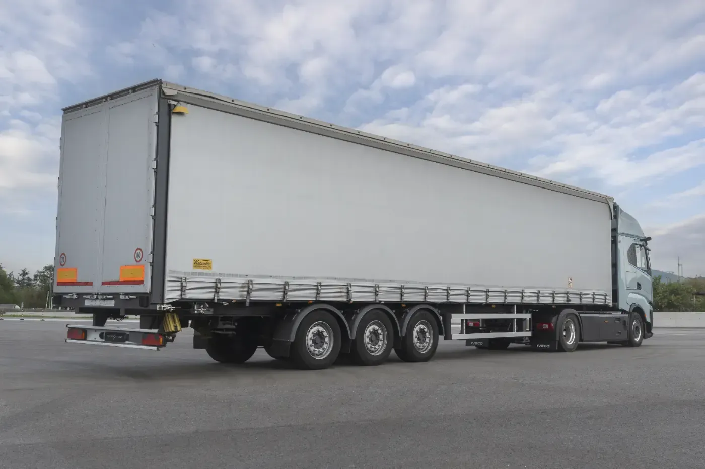 Weißer Sattelzug auf einer Straße unter bewölktem Himmel, von der Seite gesehen.