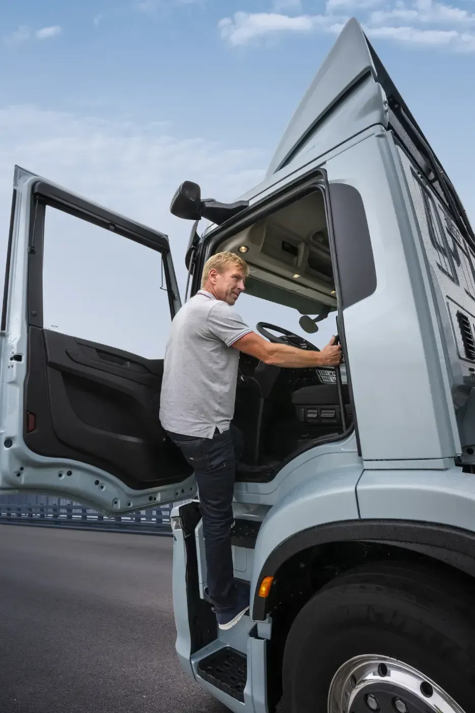 Ein Mann steigt auf der Straße in das Führerhaus eines grauen Sattelzugs, die Tür ist offen.