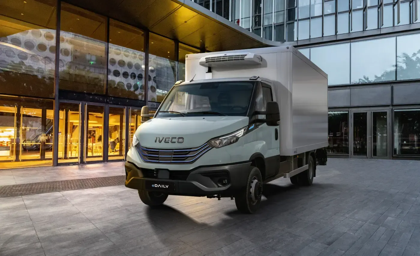 Ein weißer Iveco-Kastenwagen parkt in der Abenddämmerung vor einem modernen Glasgebäude.