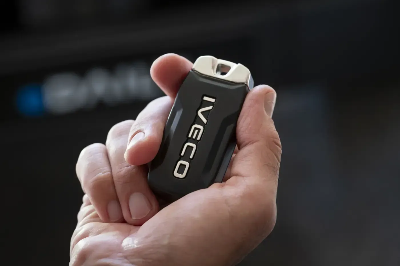 Nahaufnahme einer Hand, die ein schwarzes Iveco-Gerät mit Metallclip hält, vor verschwommenem Hintergrund
