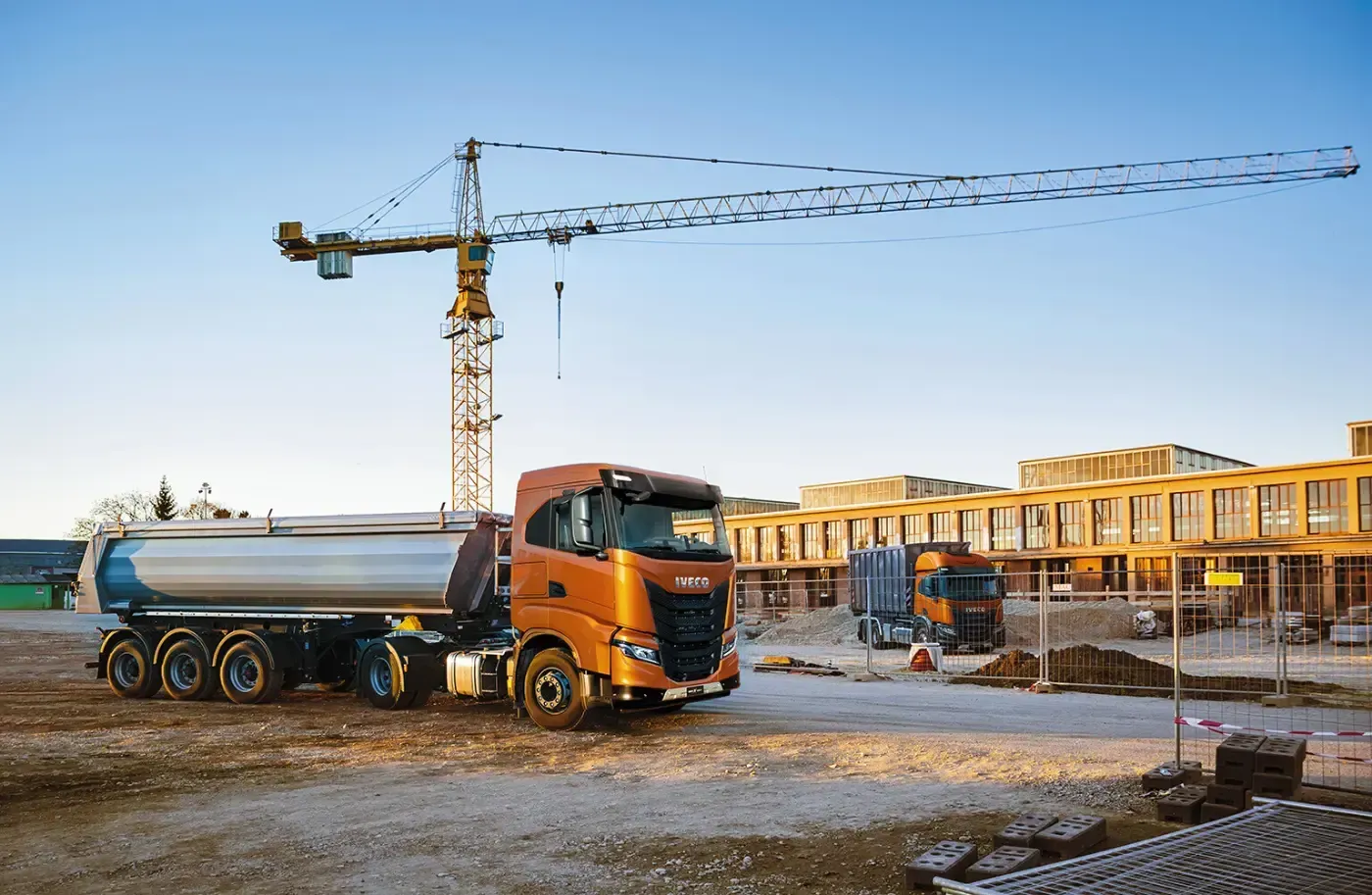 Ein orangefarbener LKW auf einer Baustelle mit Kran und unfertigen Gebäuden bei Sonnenuntergang