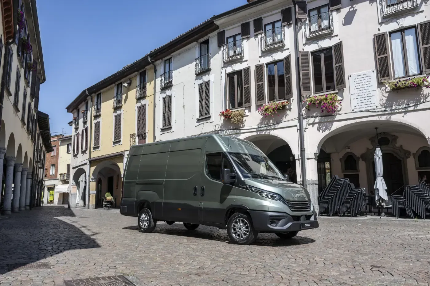 Ein dunkelgrüner Lieferwagen parkt in einer Kopfsteinpflasterstraße neben alten europäischen Gebäuden.