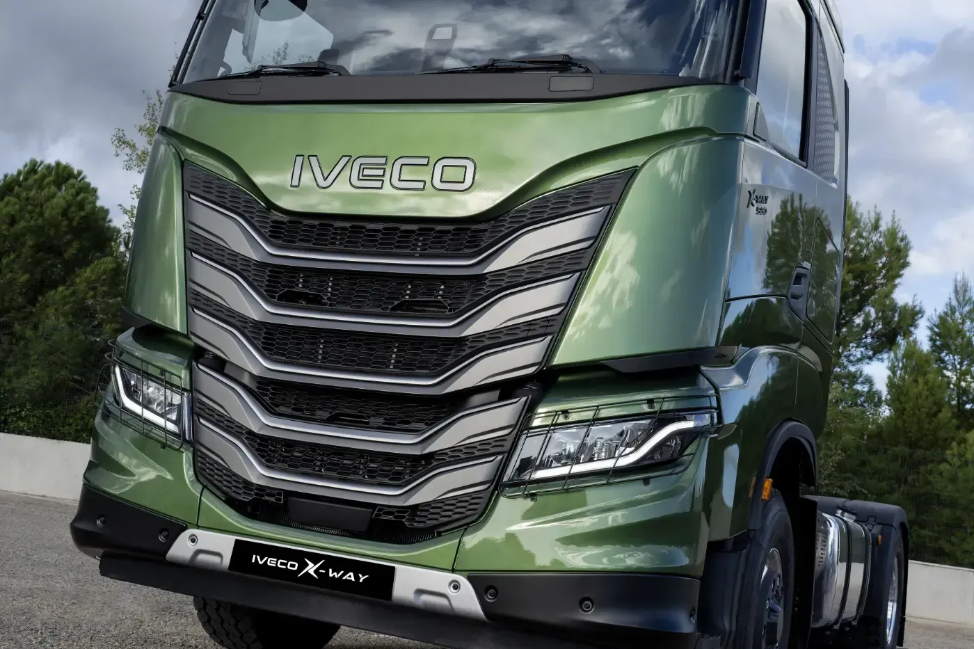Vorderansicht eines grünen Iveco-Lkw mit Chromgrill, der im Freien unter bewölktem Himmel geparkt ist