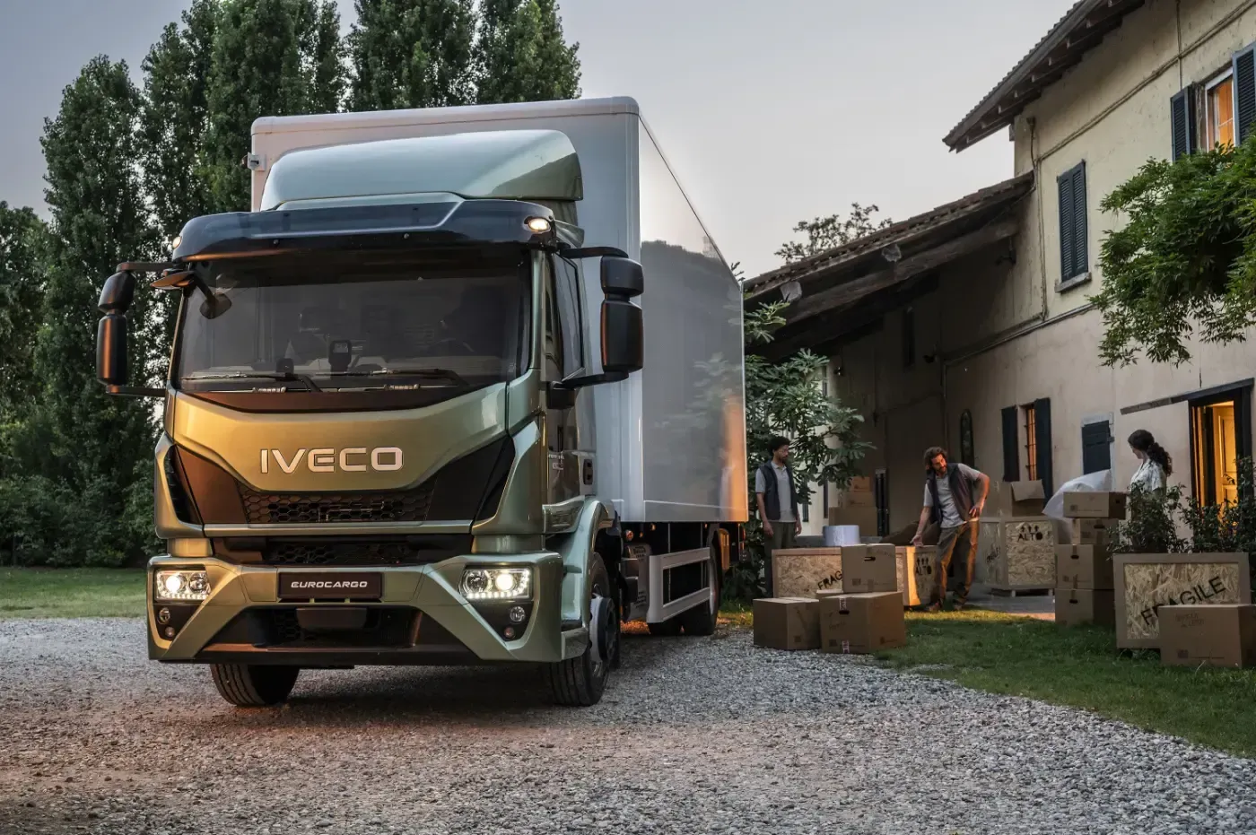 Ein grüner Iveco-Kastenwagen parkte auf einer Schotterauffahrt neben einem Bauernhaus, auf dem Kisten gestapelt waren.