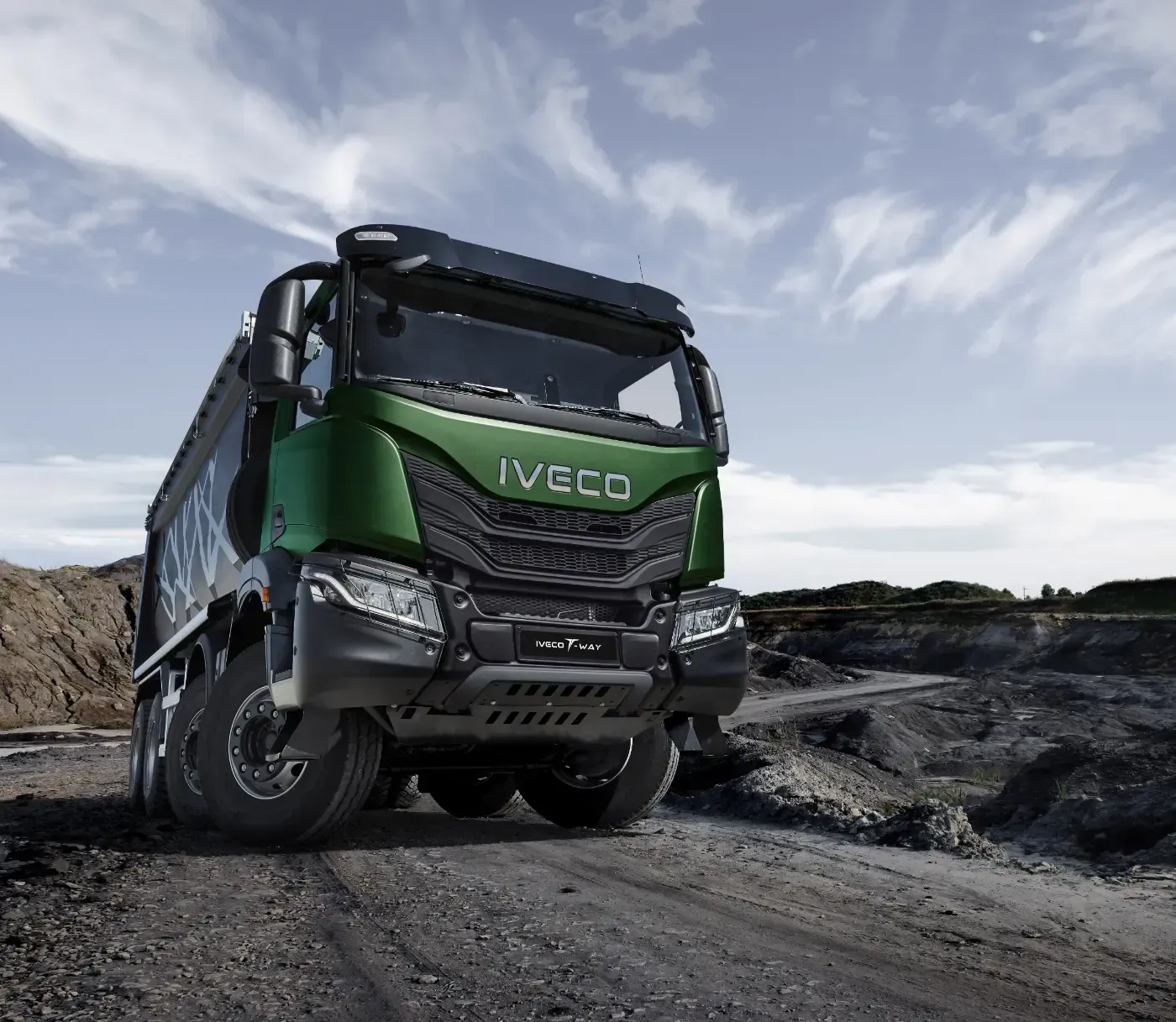 Ein grüner Iveco-Muldenkipper fährt unter bewölktem Himmel auf einer steinigen Steinbruchstraße.