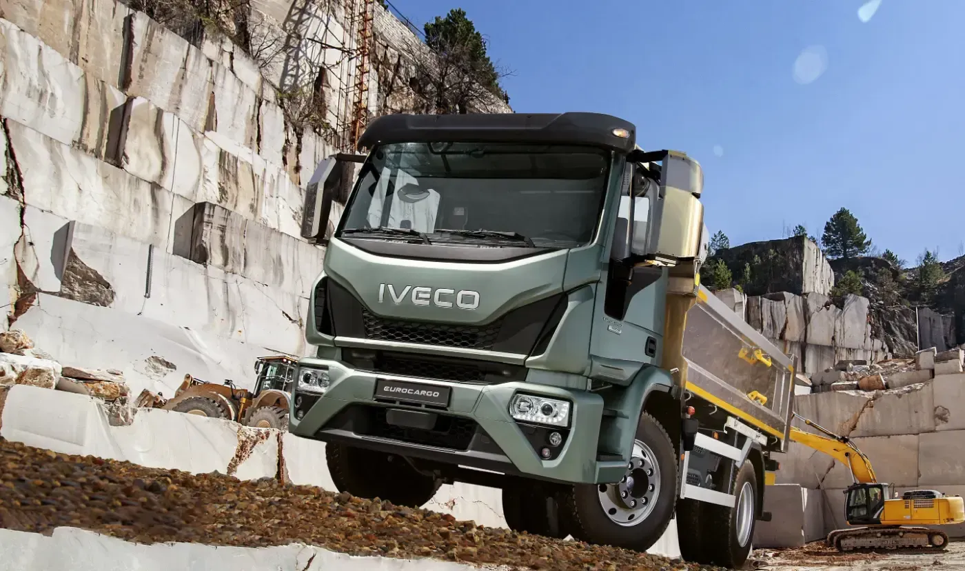 Ein grüner Iveco-Muldenkipper transportiert Gestein neben einer Steinbruchwand unter blauem Himmel