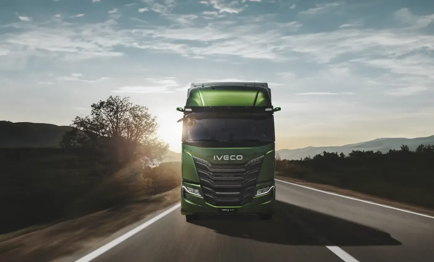Ein grüner Iveco-Sattelzug fährt bei Sonnenaufgang auf einer Autobahn.