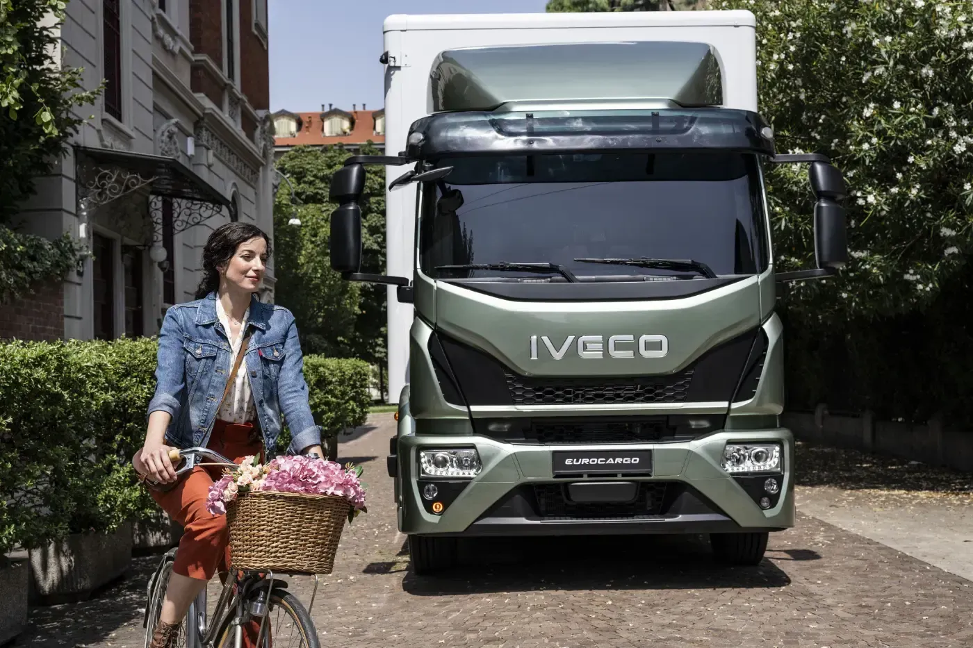 Ein Radfahrer mit Korb fährt auf einer schmalen Wohnstraße vor einem Iveco-Lkw vorbei.
