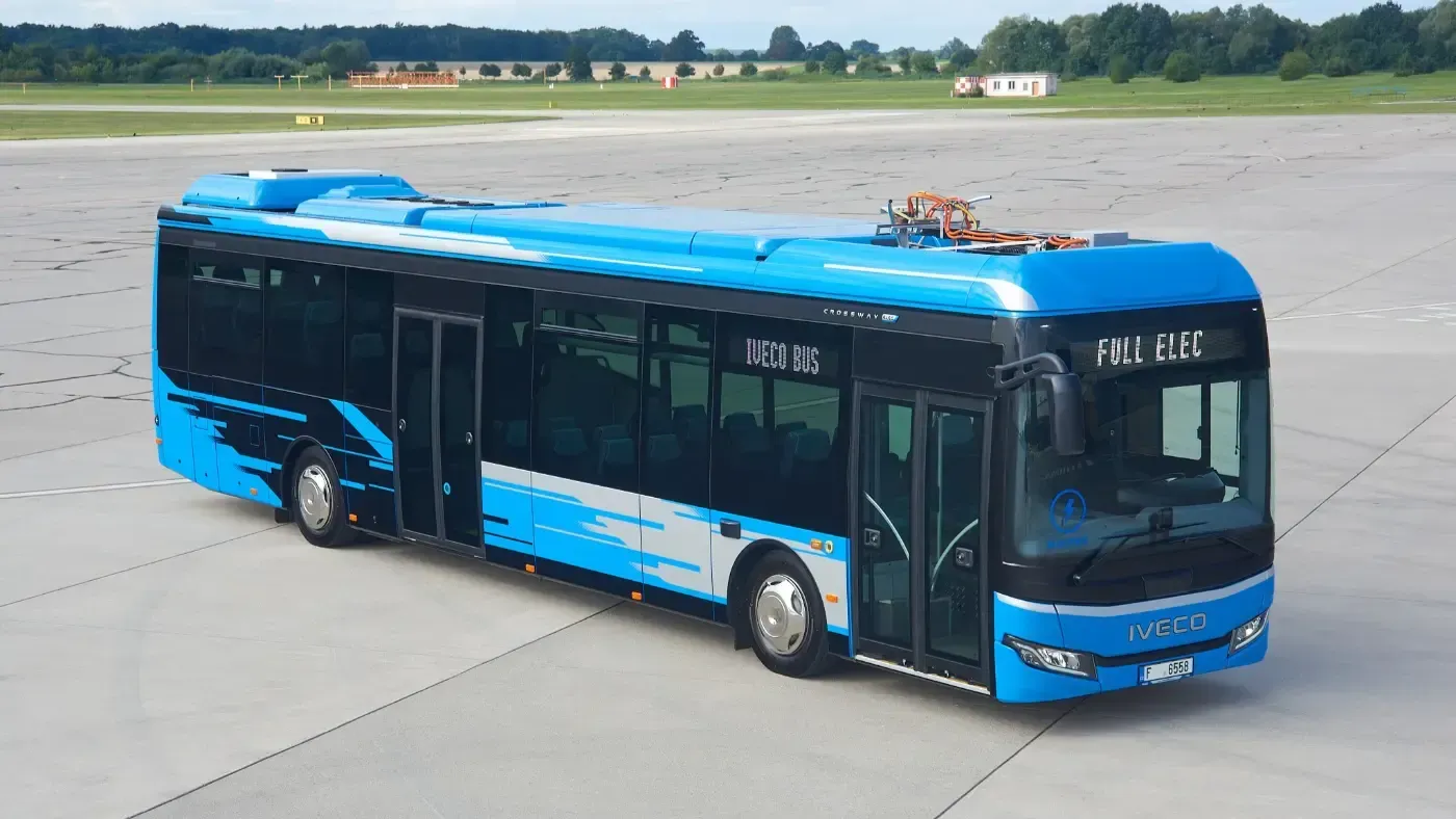Blauer Stadtbus auf einem gepflasterten Parkplatz, von oben schräg betrachtet.