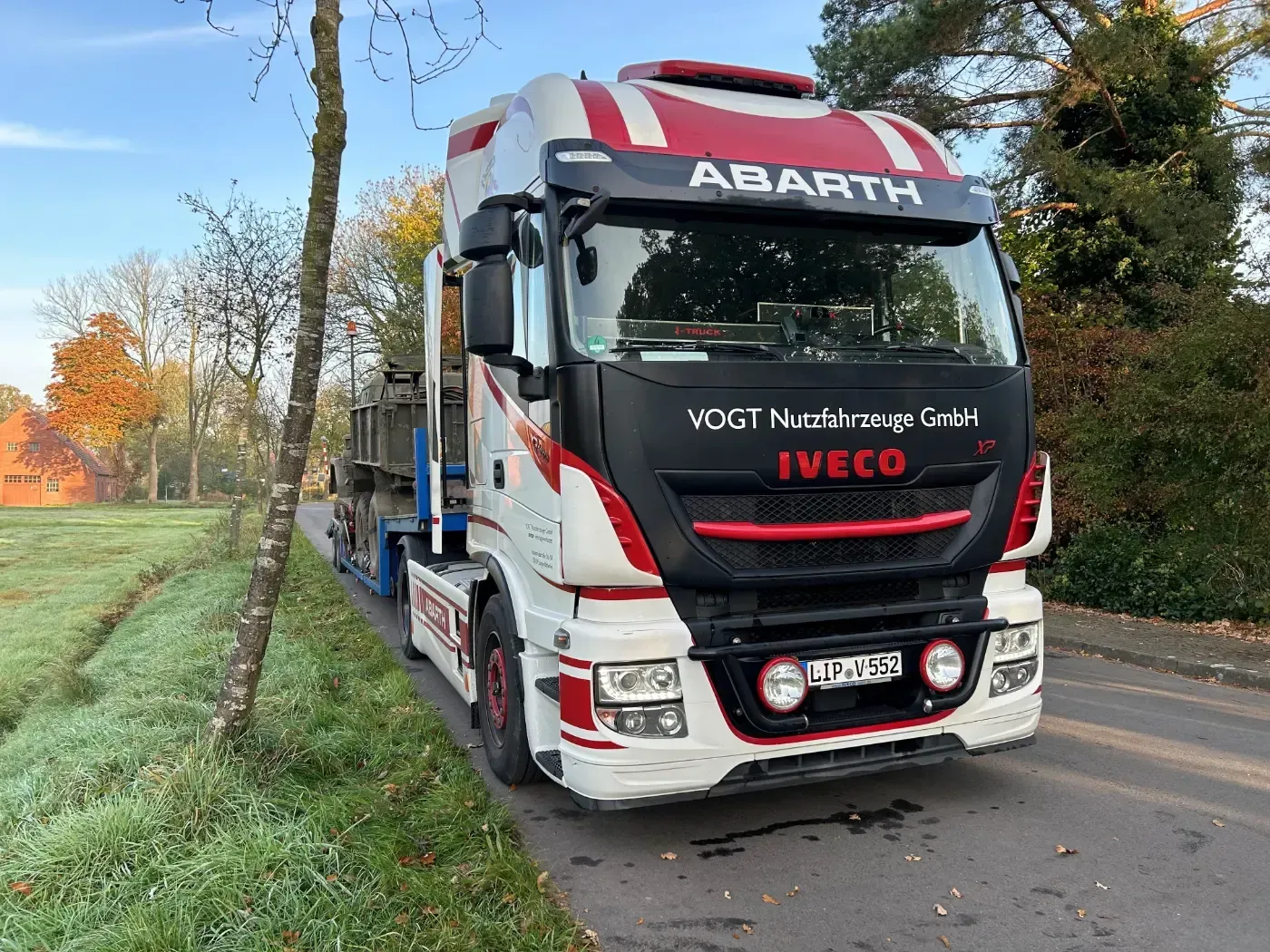 Ein roter und weißer Abarth Iveco-Lkw parkt im Herbst am Straßenrand neben Gras und Bäumen.