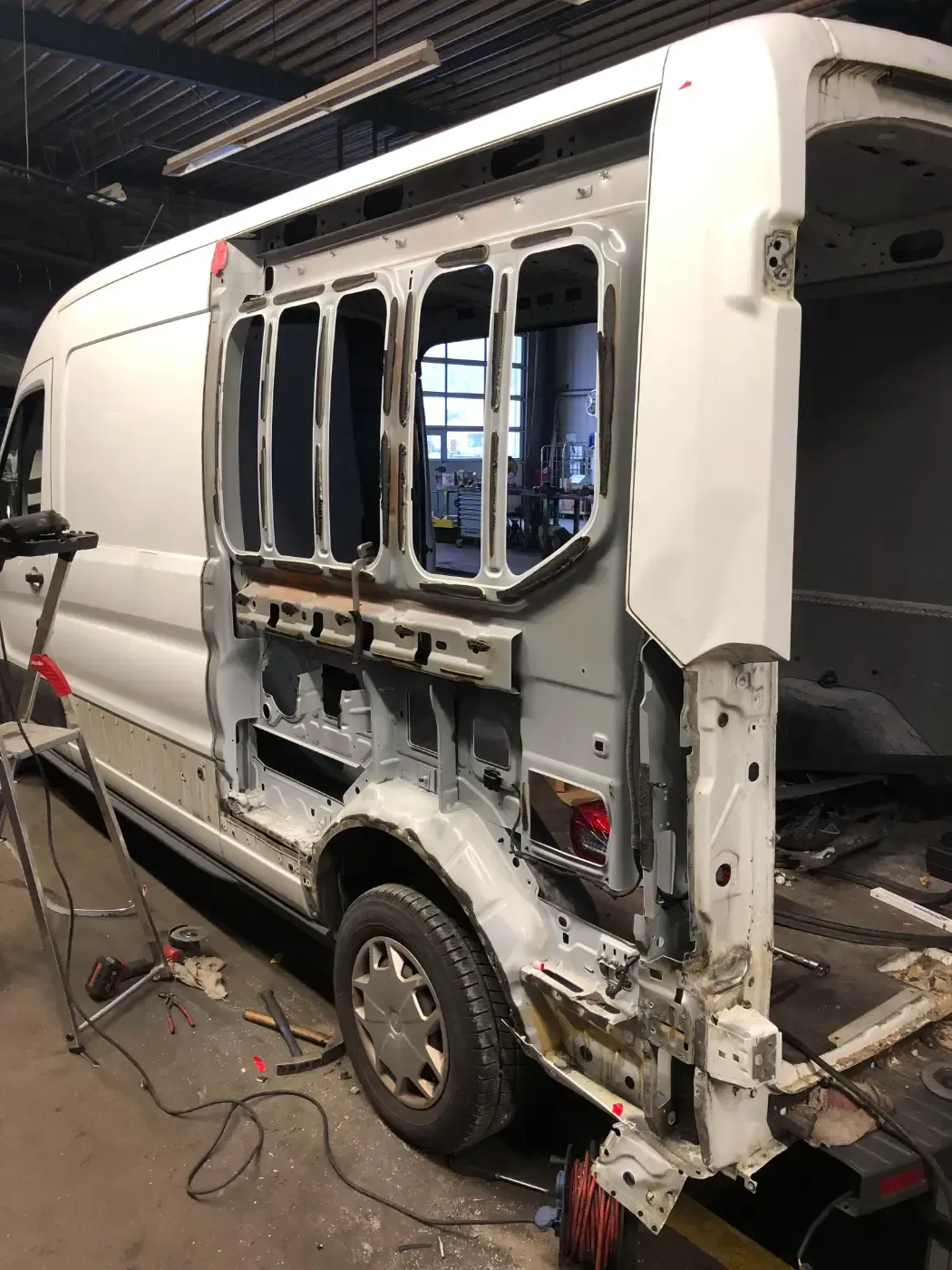 Weißer Lieferwagen mit abgenommener Seitenwand, Rahmen und Fenster sind freigelegt, in einer Garage oder Werkstatt.