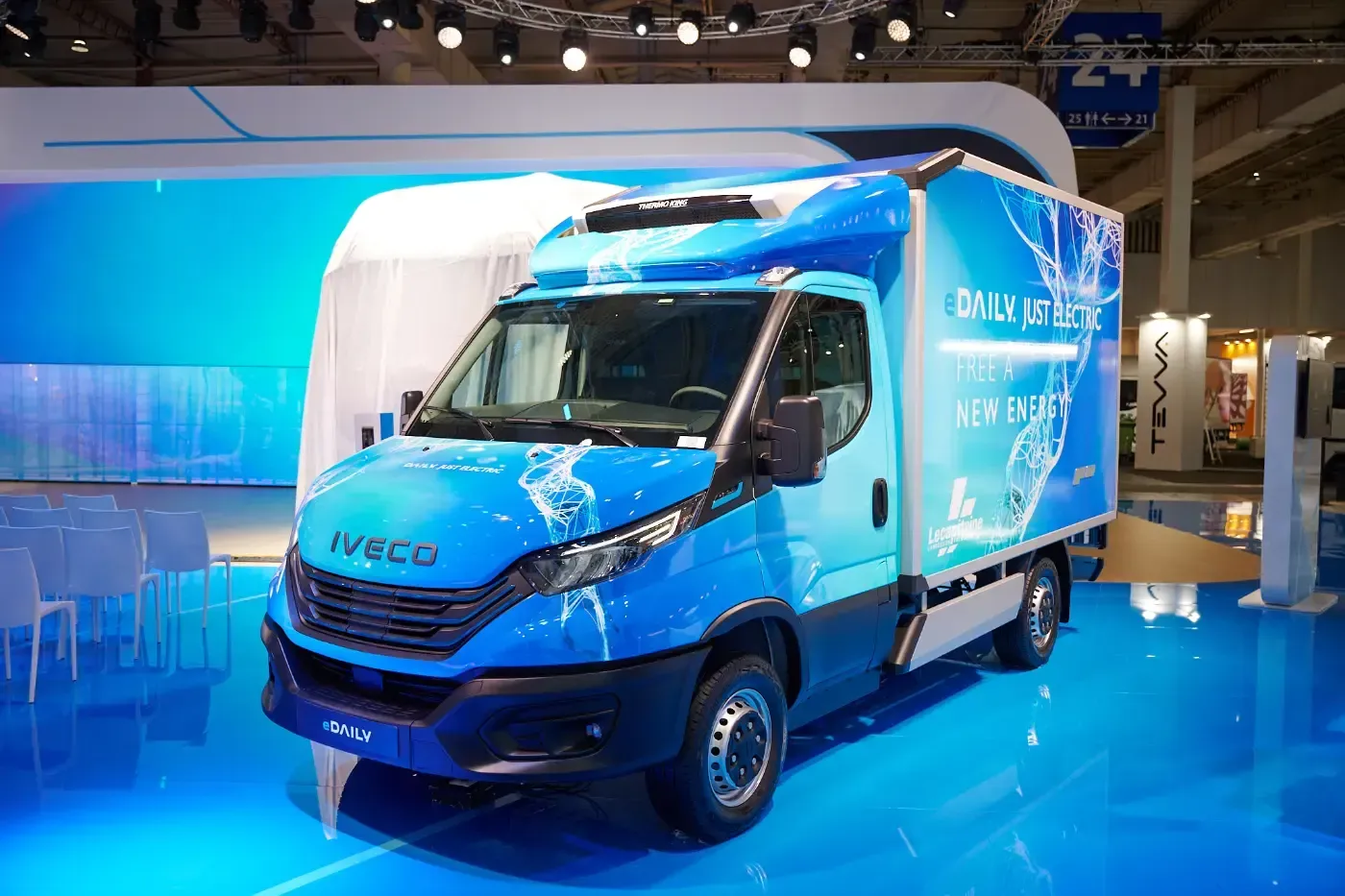 Ein blauer Lieferwagen mit weißem Laderaum und glänzendem Boden wird in einer Automobilhalle ausgestellt.