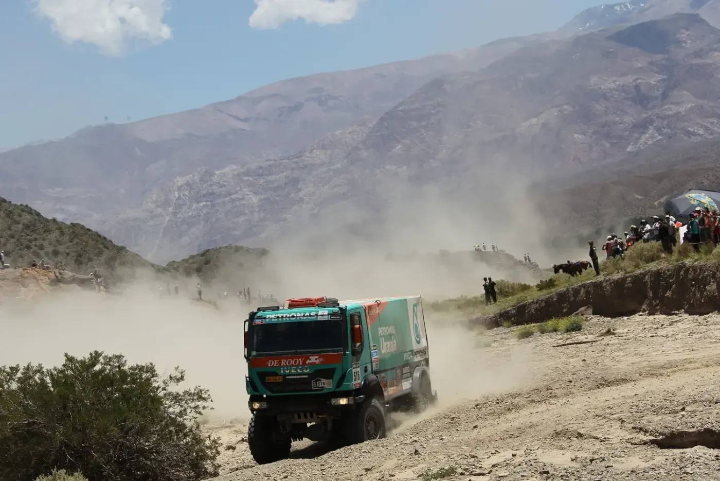 Ein grüner Truck rast auf einer staubigen Bergstraße, umgeben von Zuschauern und aufgewirbeltem Staub.