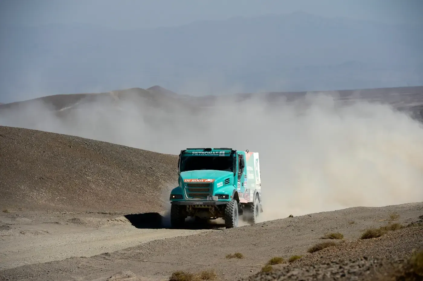 Türkisfarbener LKW fährt durch eine staubige Wüstenlandschaft