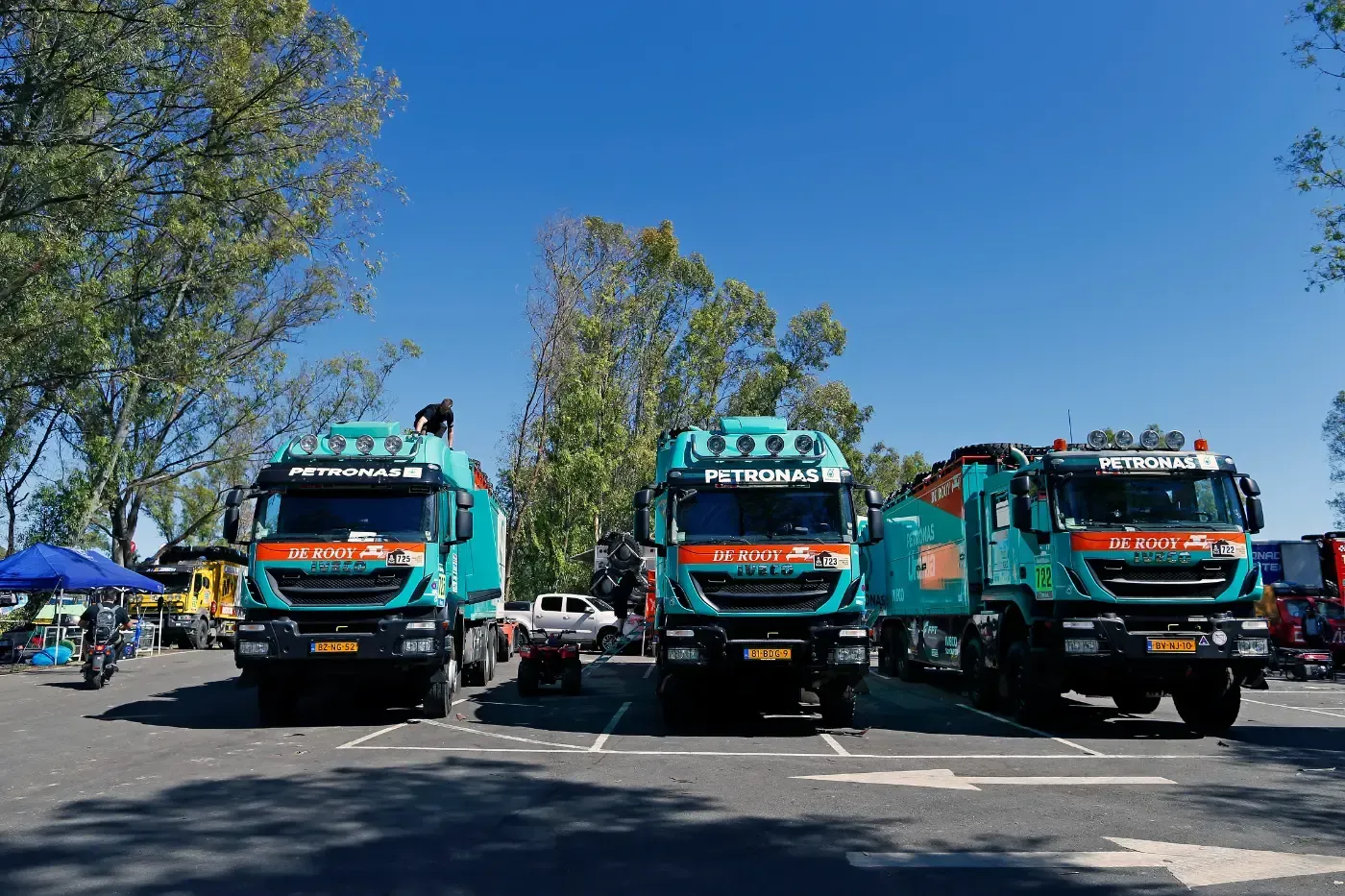 Drei türkisfarbene Lieferwagen parkten nebeneinander auf einer sonnigen Straße unter klarem, blauem Himmel.