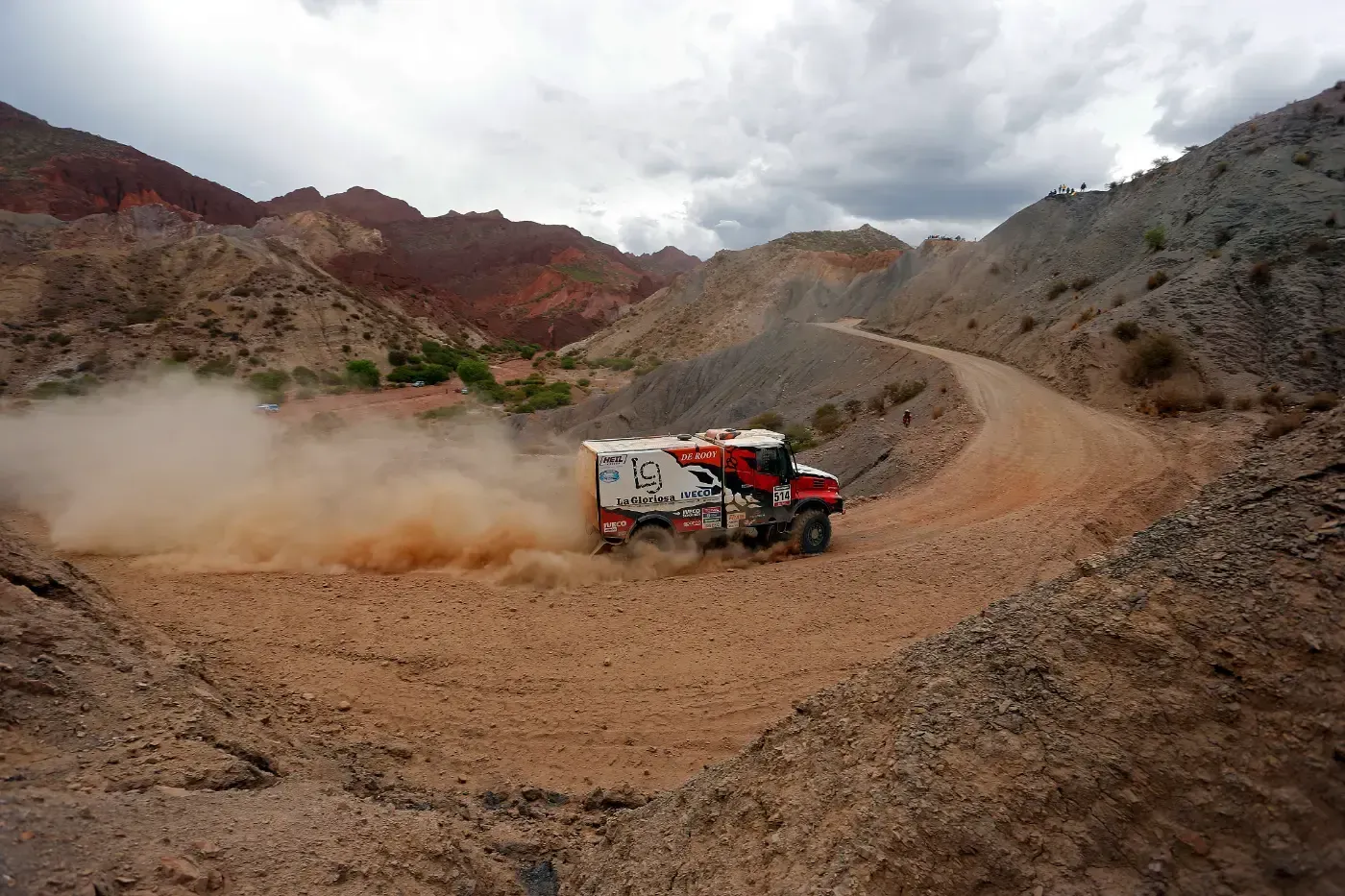 Ein Offroad-Rallye-Truck wirbelt Staub auf einem felsigen Wüstenbergpfad auf.