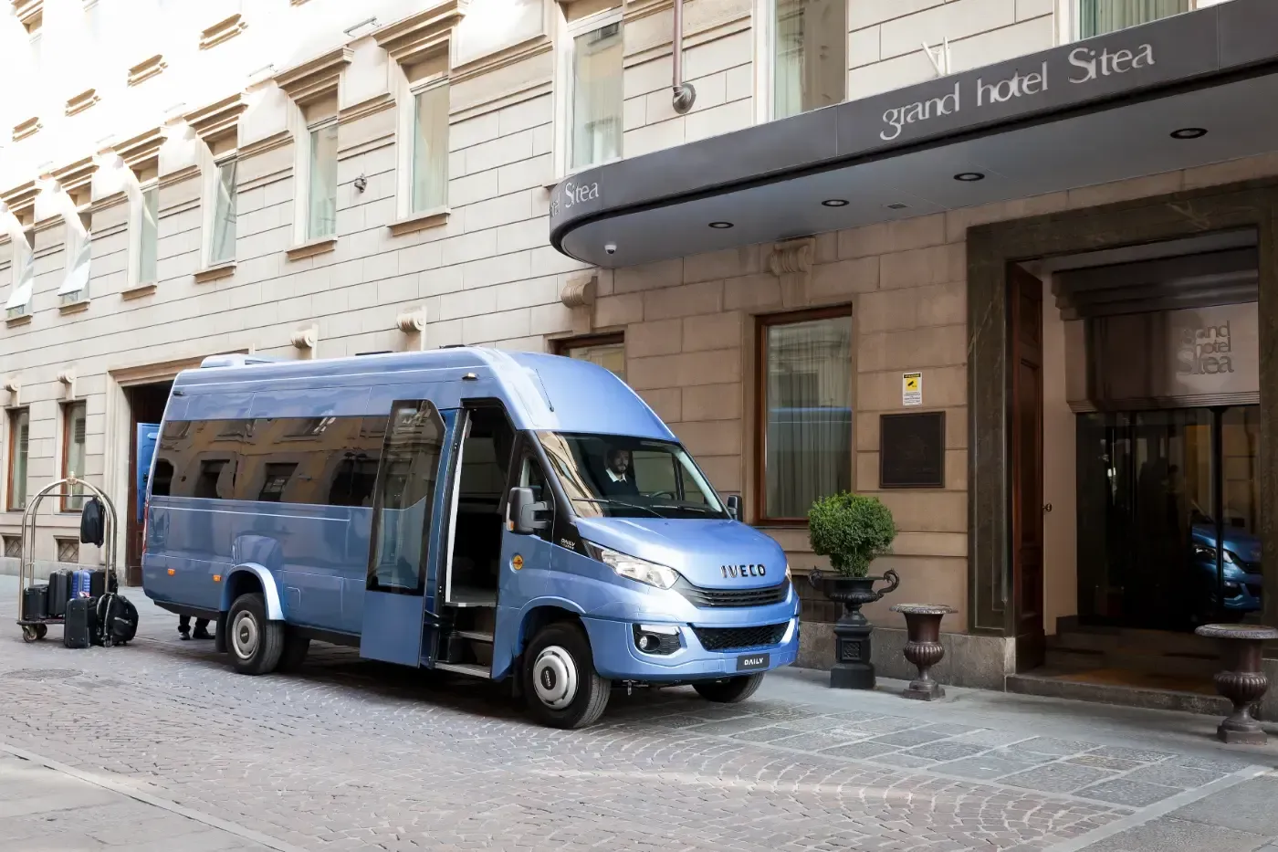 Ein blauer Lieferwagen parkte vor dem Hoteleingang in einer Kopfsteinpflasterstraße.