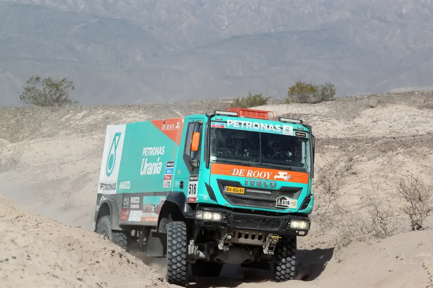 Türkisfarbener Rallye-Truck rast über eine staubige Offroad-Wüstenstrecke