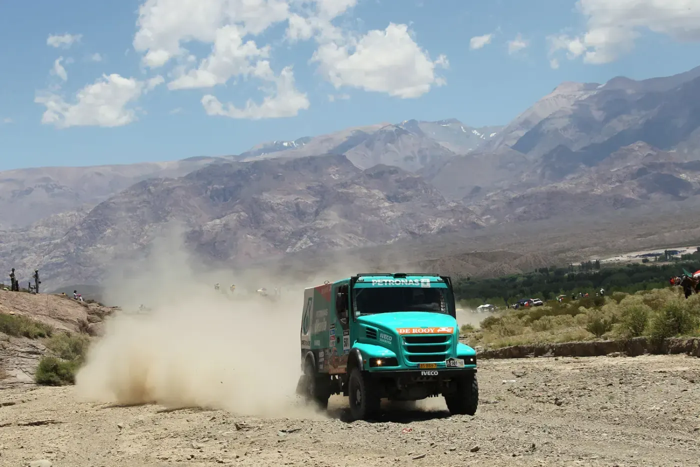 Ein türkisfarbener Truck raste mit einer Staubwolke hinter sich auf einer staubigen Bergstraße.