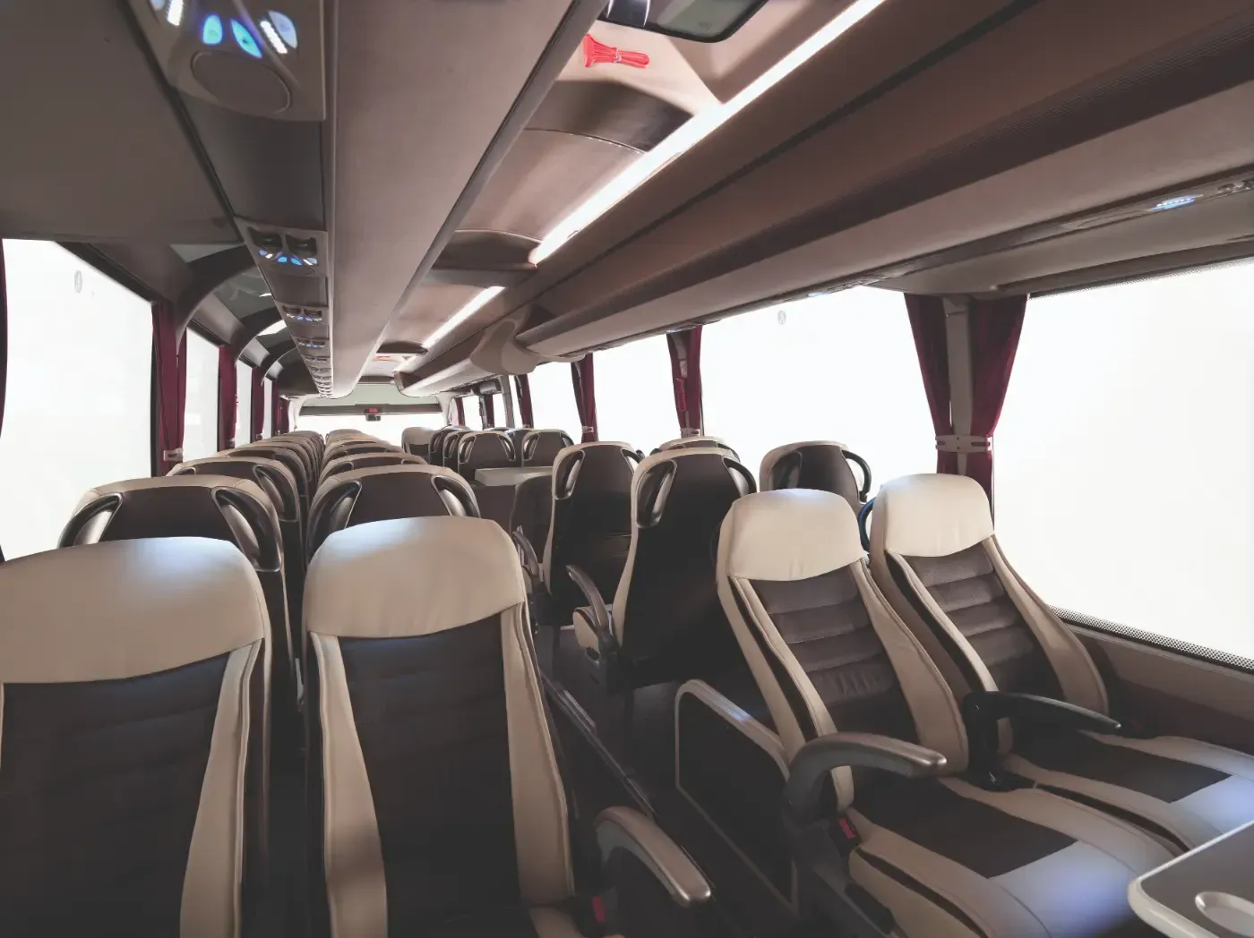 Innenraum eines leeren Reisebusses mit Reihen grau-schwarzer Sitze und großen Seitenfenstern.
