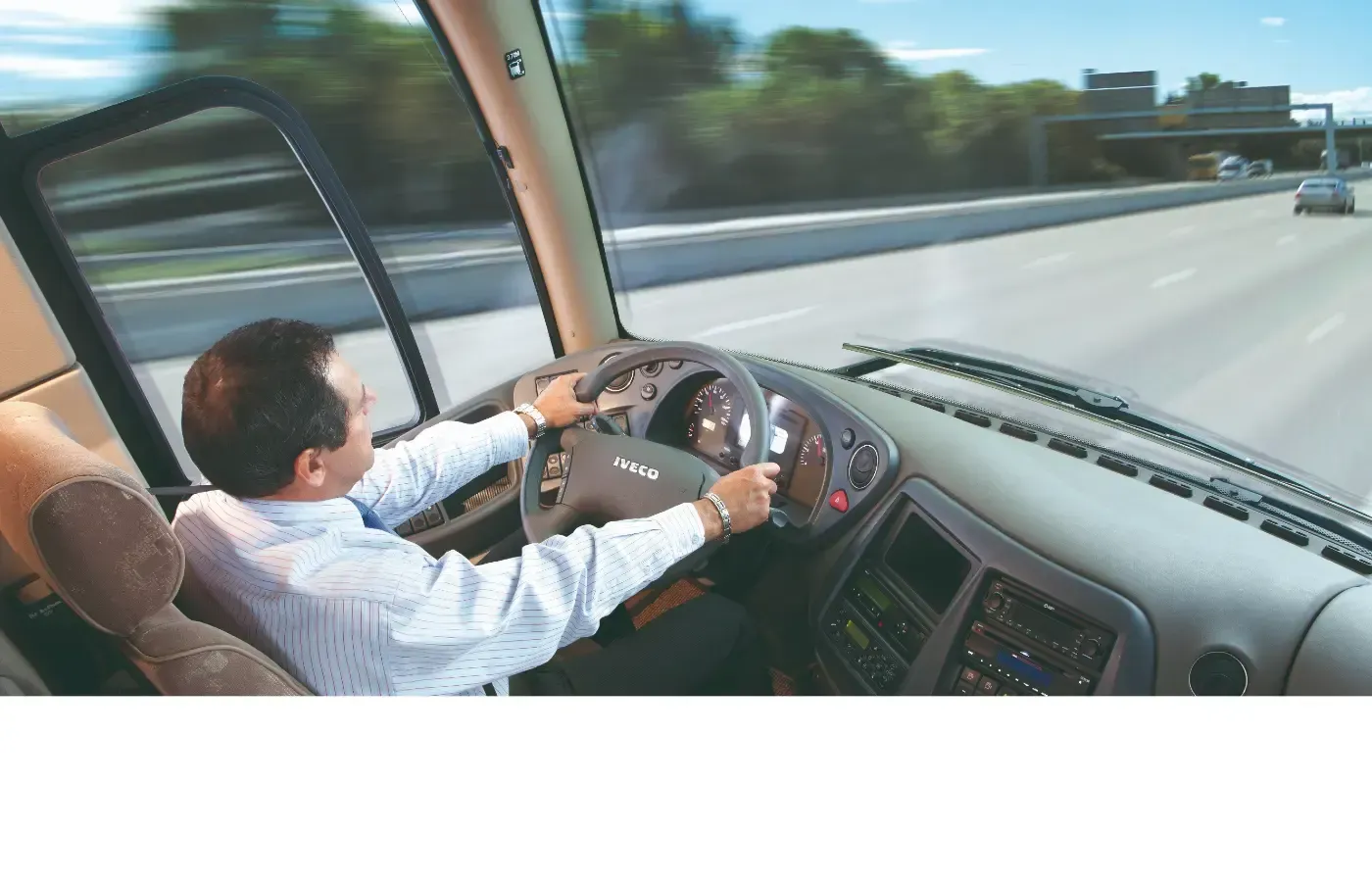 Ein Mann fährt Bus auf einer Autobahn, Hände am Lenkrad, Straße vor sich sichtbar.