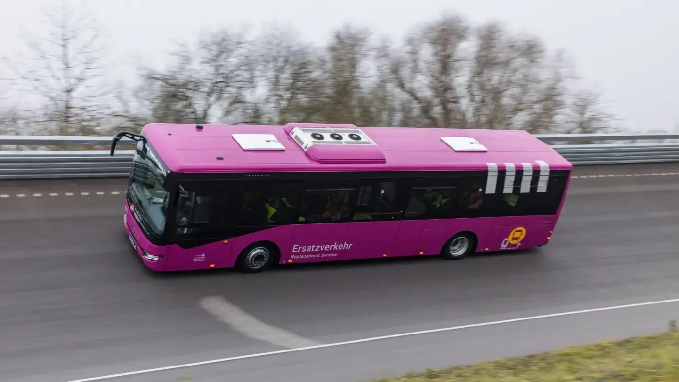 Ein leuchtend pinkfarbener Reisebus fährt auf einer Autobahn, von der Seite in Bewegung gesehen.