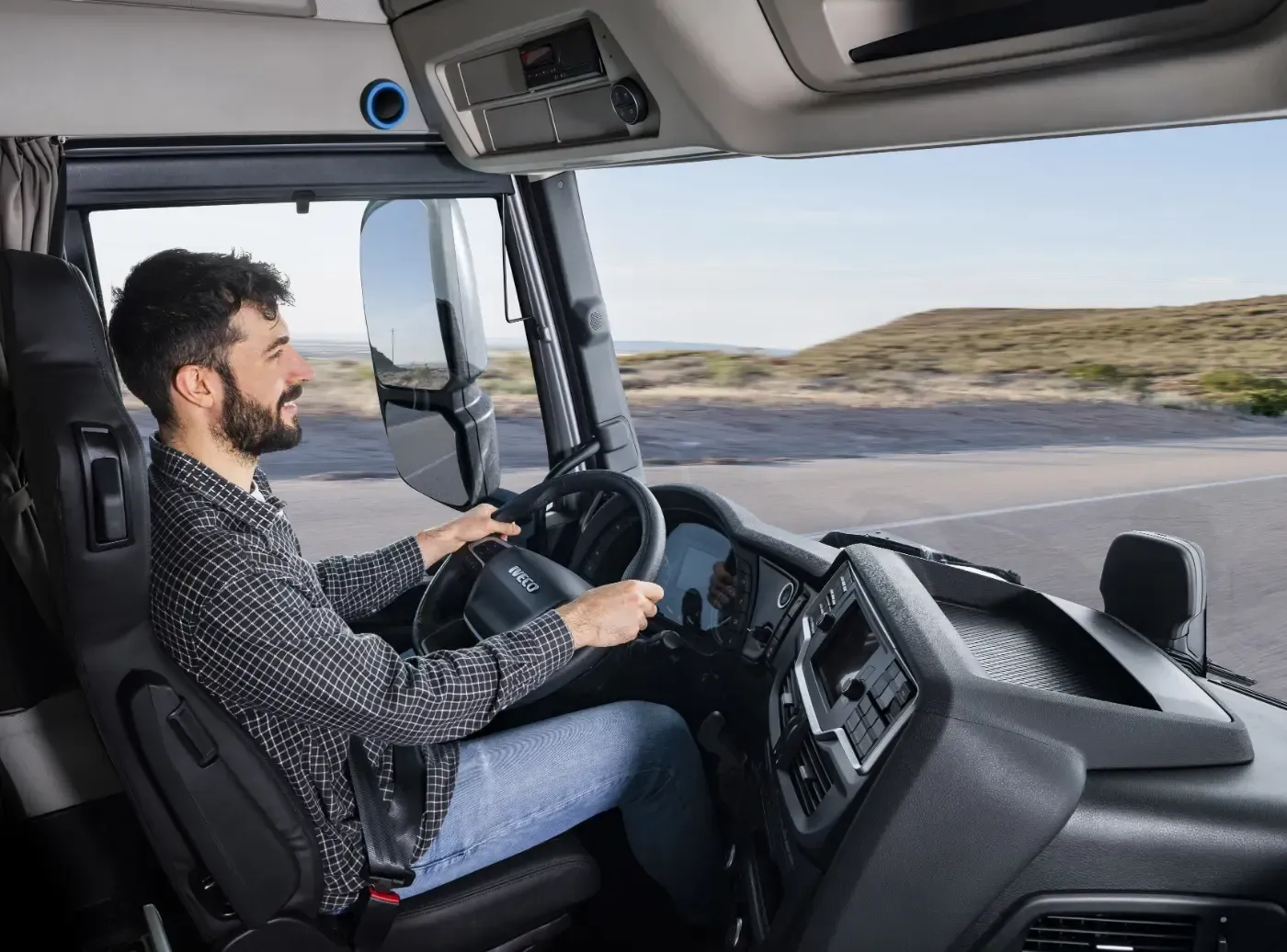 Fahrer steuert einen Lastwagen auf einer Wüstenstraße, Aufnahme vom Beifahrersitz aus, draußen offene Landschaft.
