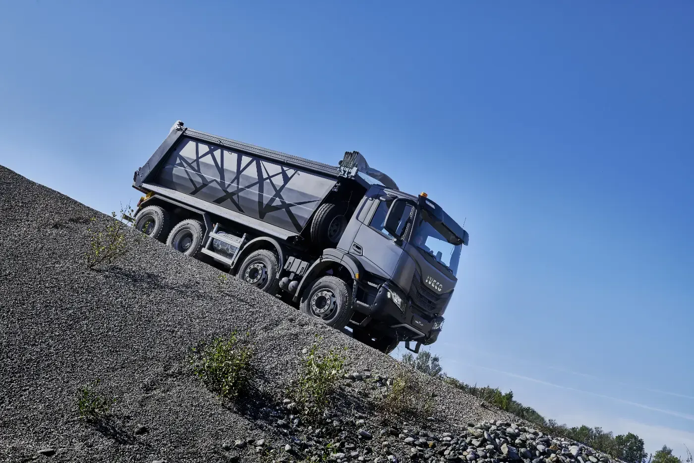 Ein Muldenkipper transportiert Kies unter strahlend blauem Himmel einen steilen Haufen hinauf.