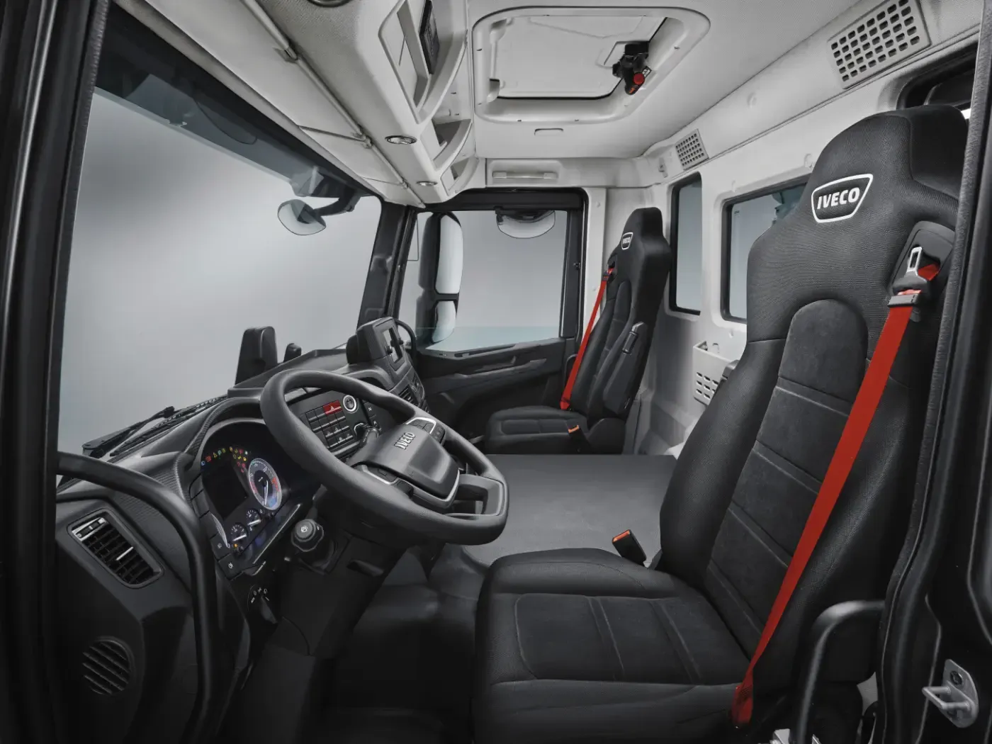 LKW-Fahrerhaus-Interieur mit schwarzen Sitzen, roten Akzenten und Lenkrad, von der Beifahrerseite aus gesehen