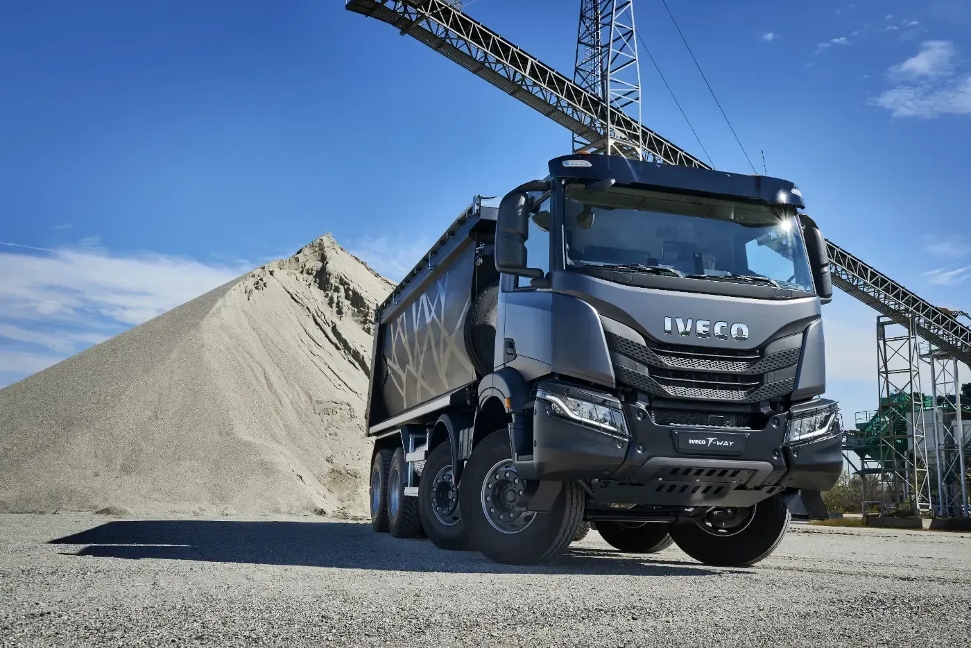 Ein blauer Muldenkipper, beladen mit Kies, steht auf einer Baustelle unter einem Kran.