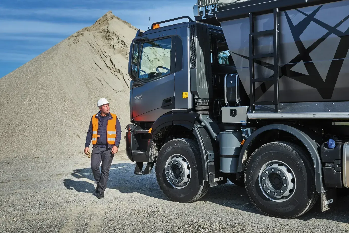 Ein Arbeiter in Schutzausrüstung geht neben einem großen Muldenkipper in einer Kiesgrube.