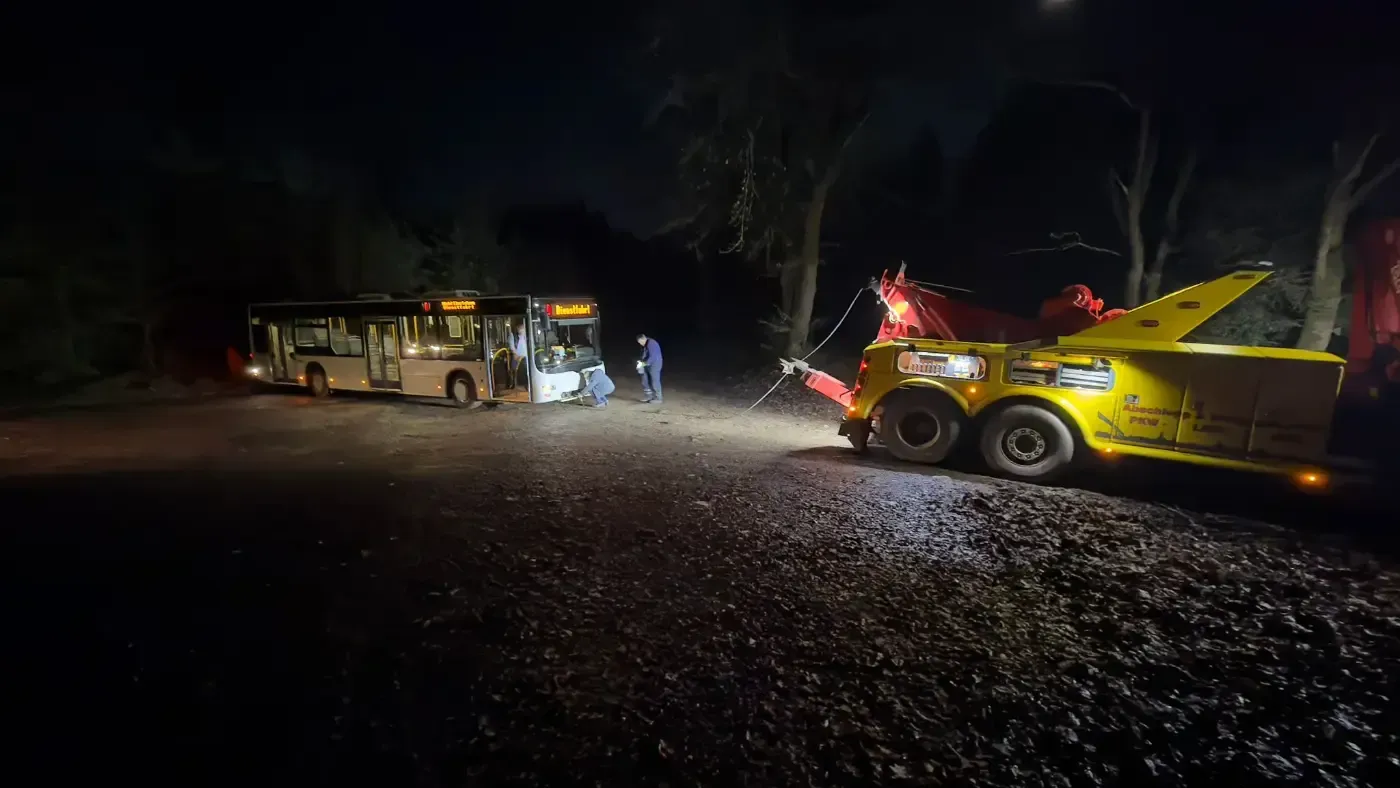Abschleppwagen und Bus parkten nachts auf einer dunklen Schotterstraße, Scheinwerfer erhellten die Szene