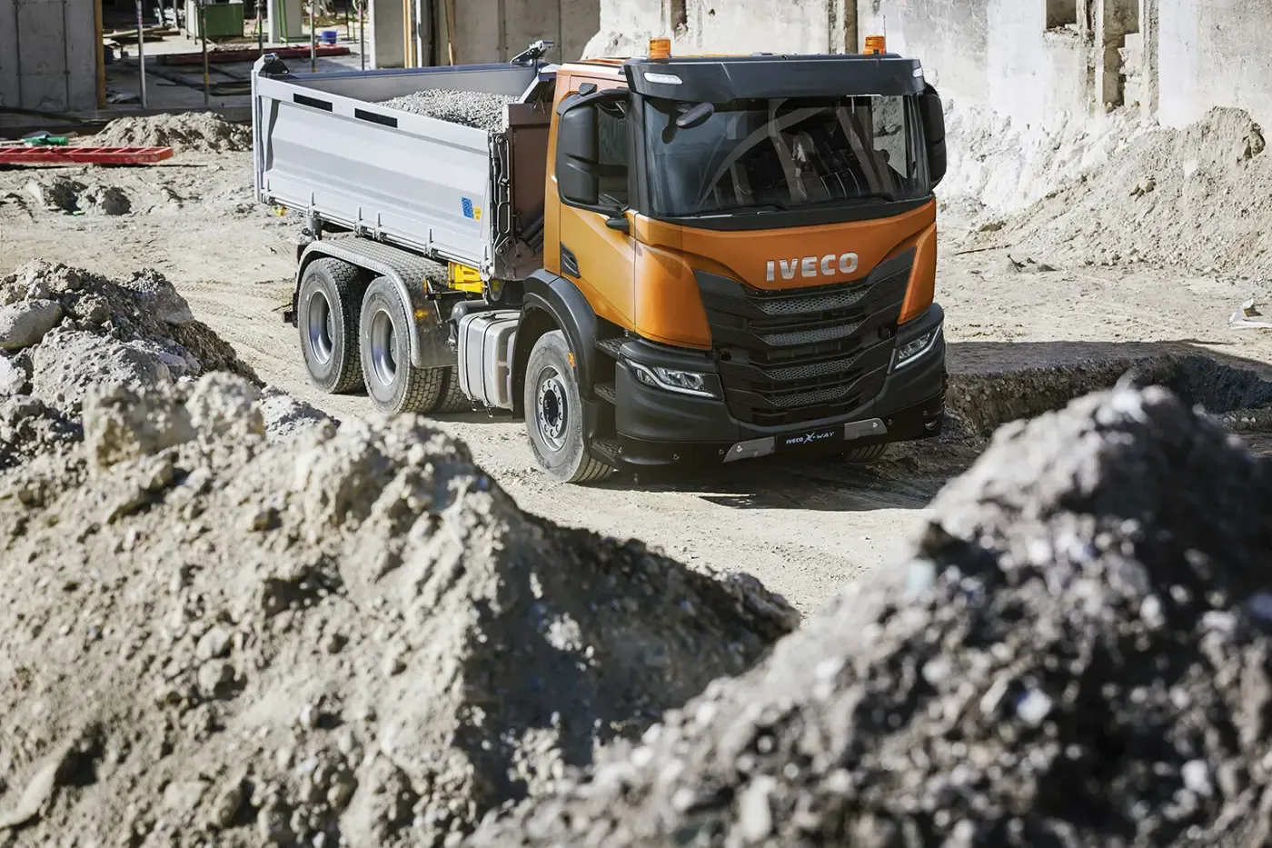 Ein orangefarbener Muldenkipper transportiert Kies in einem Steinbruch, umgeben von Haufen hellen Gesteins.