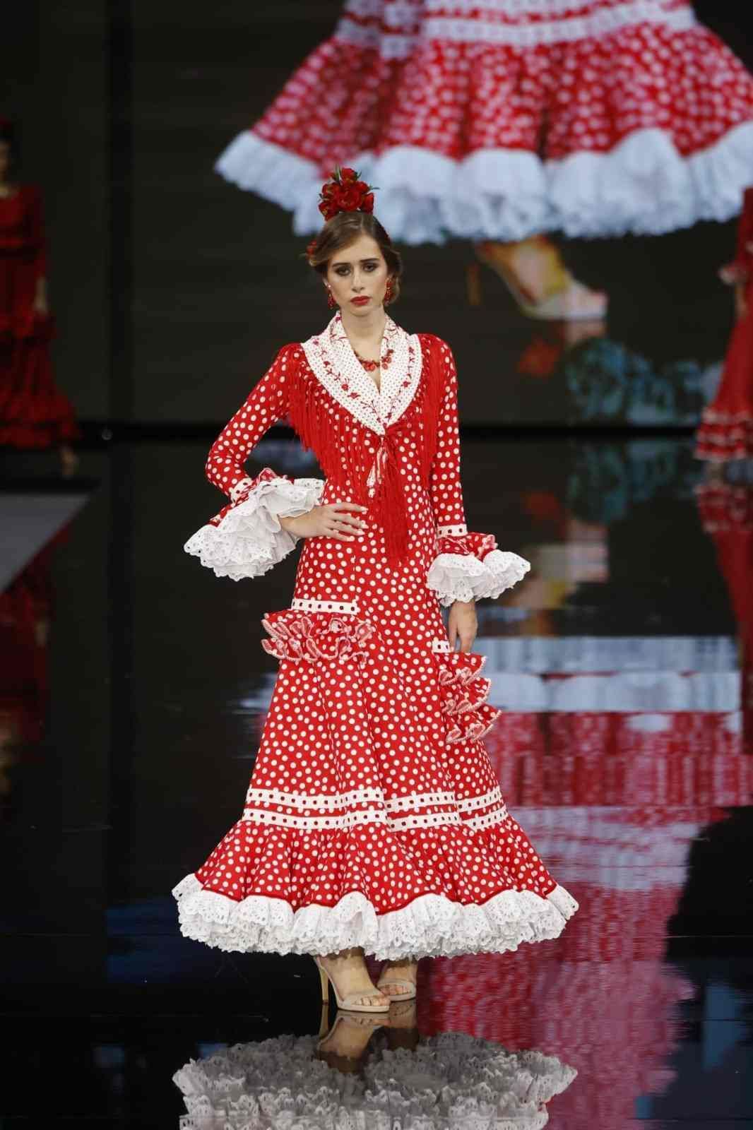Modelo con un vestido rojo de lunares con volantes blancos desfilando en una pasarela durante un desfile de moda.