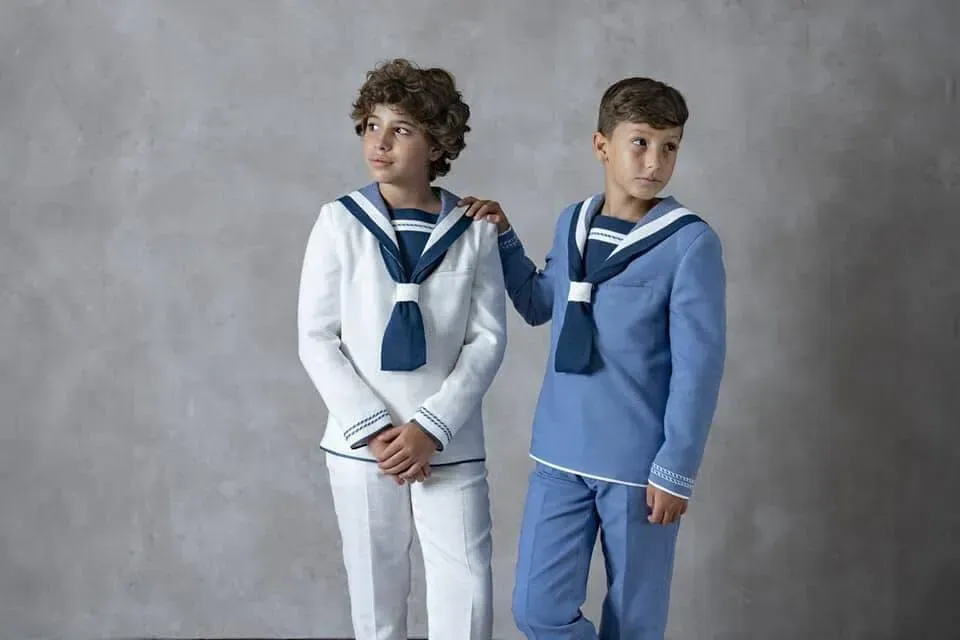 Dos niños vestidos con trajes de marinero azul marino y blanco posan frente a un fondo de estudio gris.