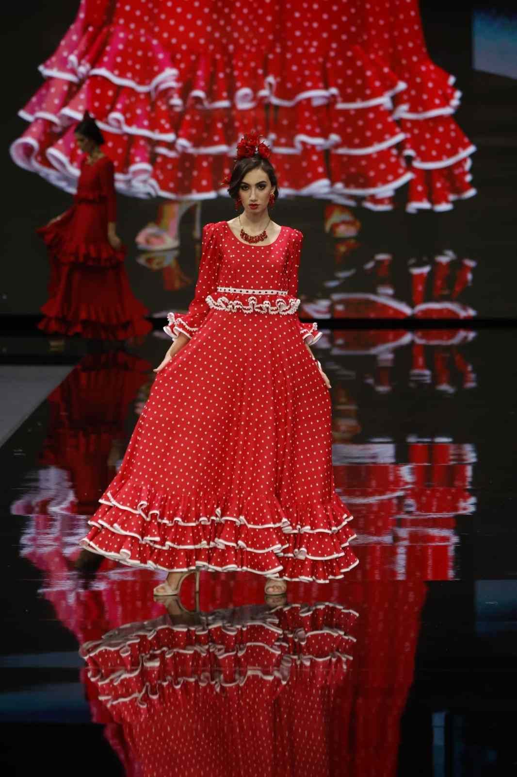 Modelo desfilando con un vestido rojo brillante de lunares con volantes, ribete blanco y dobladillo reflectante.