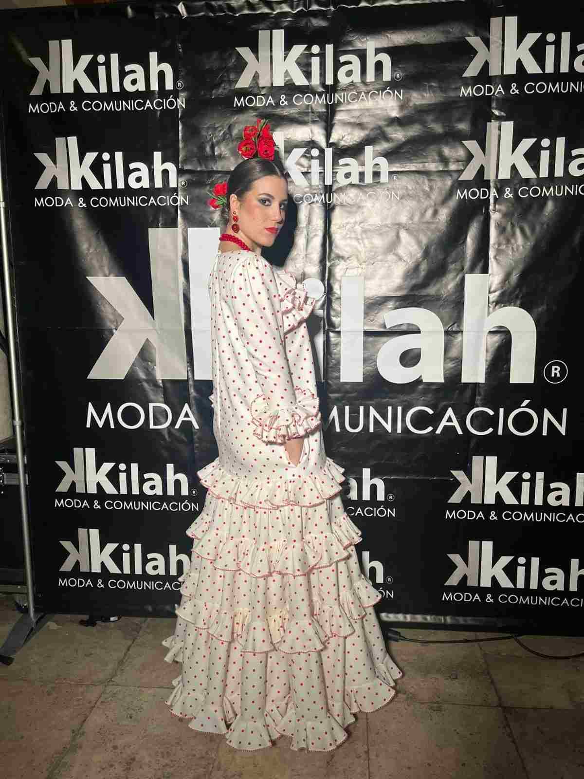 Mujer con un vestido blanco con volantes posando frente a un telón de fondo de Kilah Moda Comunicación.