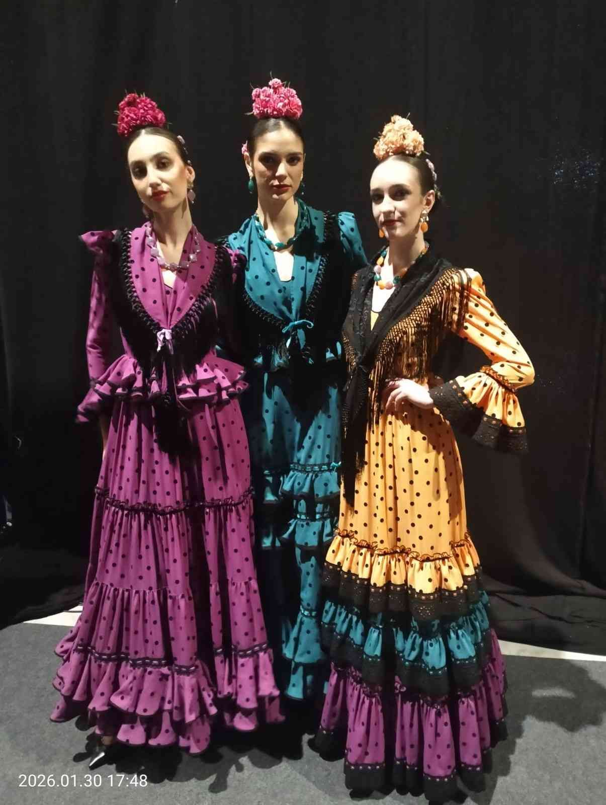 Tres bailarinas con coloridos vestidos de flamenco posan frente a un fondo oscuro.
