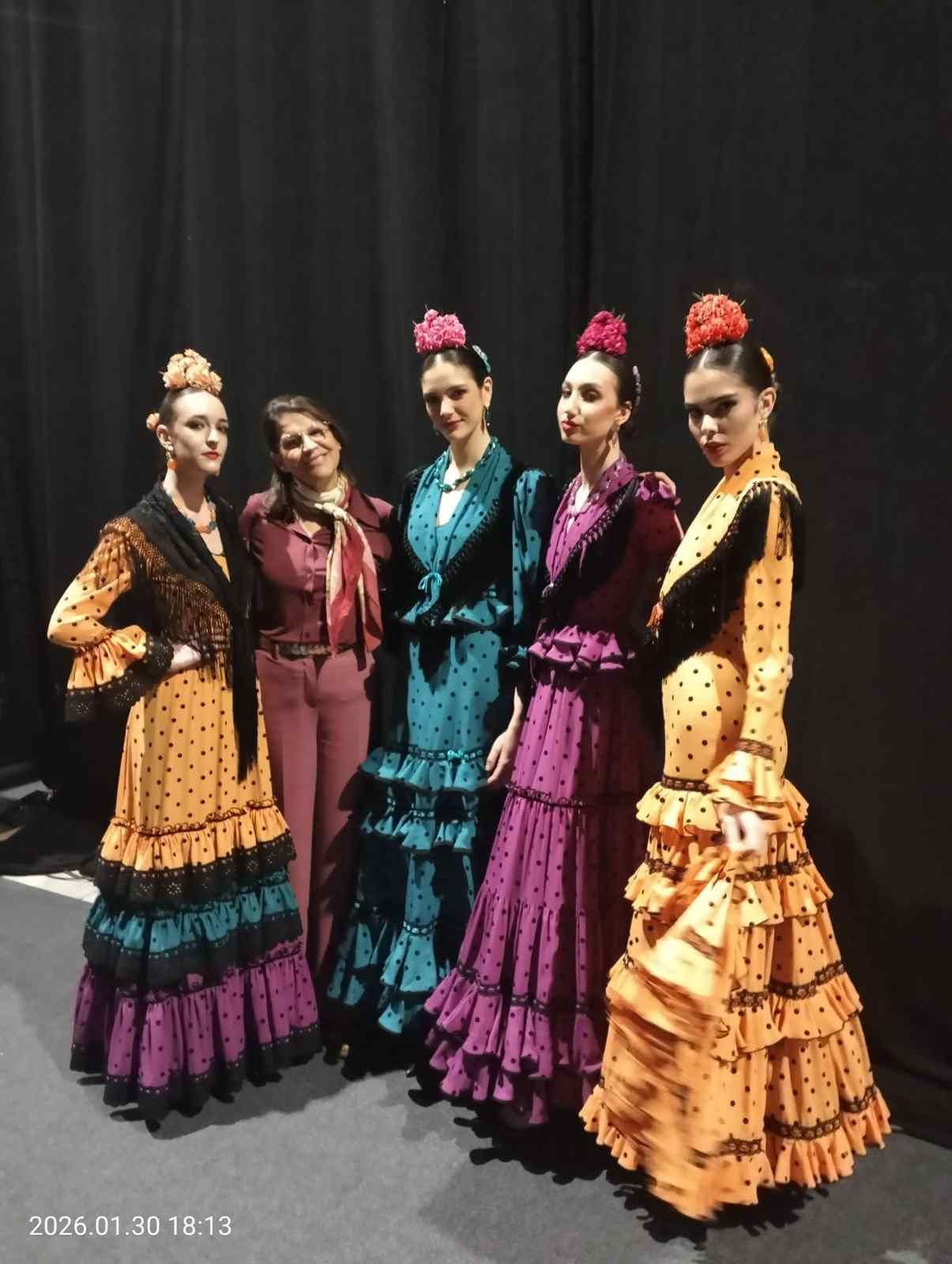 Cinco bailarinas con coloridos trajes de flamenco posando frente a una cortina negra.