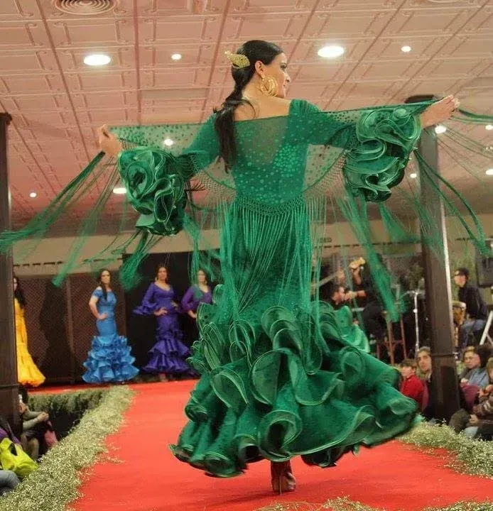 Una modelo con un vestido verde con volantes desfila por una pasarela con bailarinas.