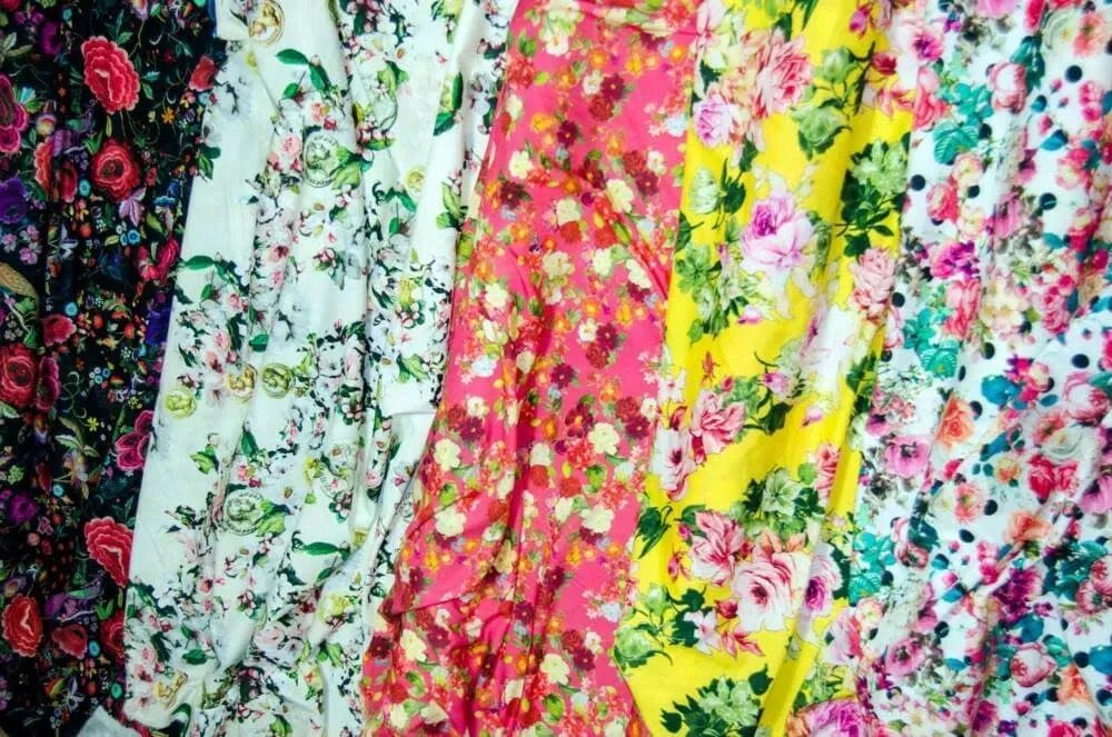 Telas florales coloridas colgadas en filas, con estampados en rosa, amarillo, blanco y tonos oscuros.