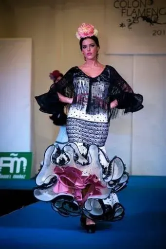 Modelo de pasarela con un vestido blanco y negro con dobladillo floral rosa y tocado a juego.