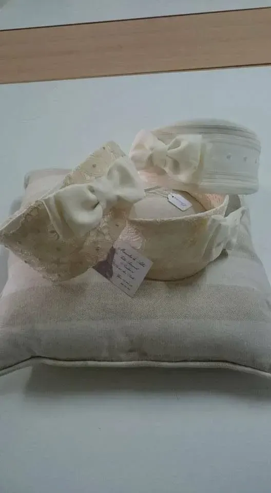 Un par de zapatos de bebé color crema con gorrito a juego sobre un cojín blanco, expuestos en el interior.