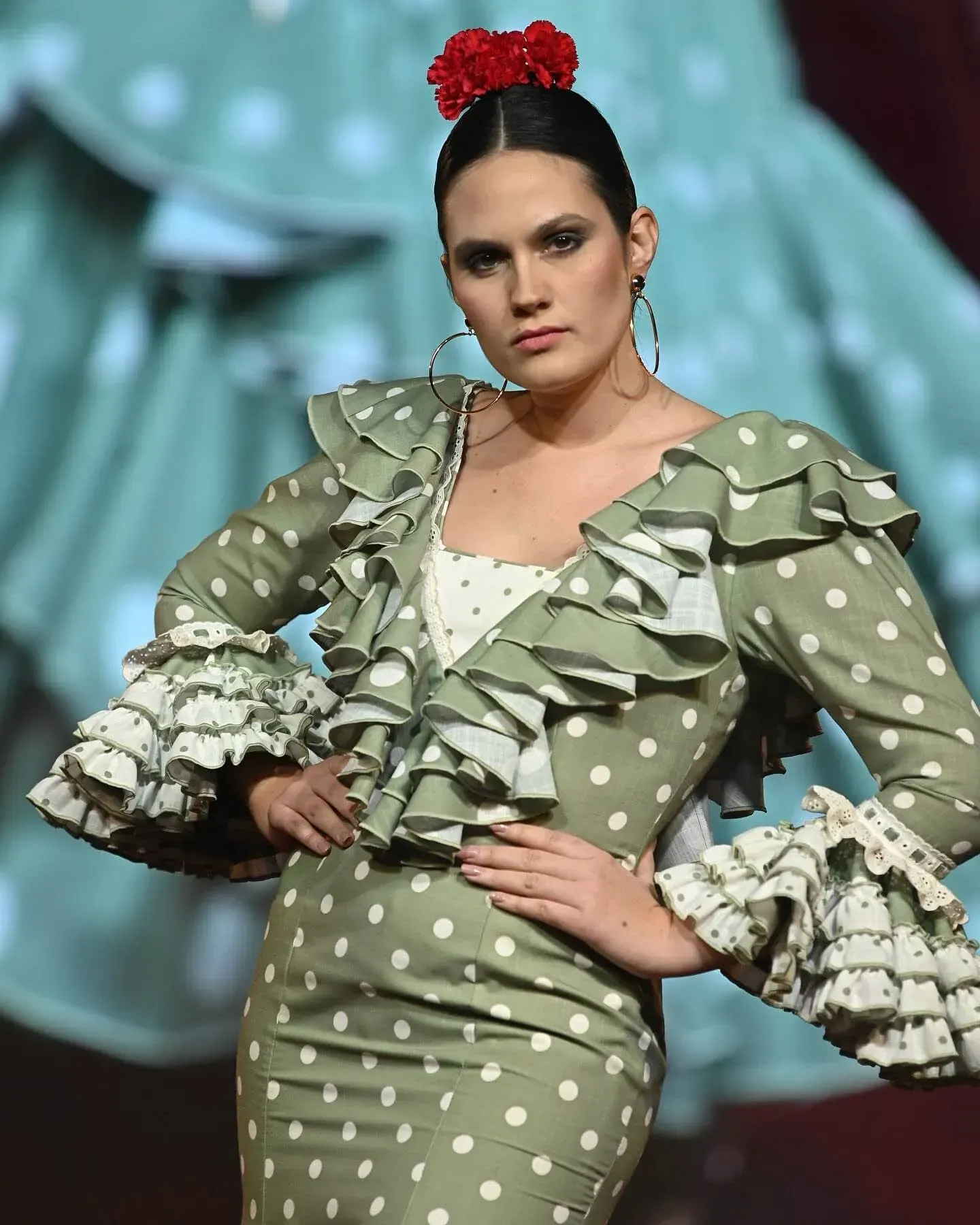 Modelo con un vestido verde oliva de lunares y volantes posando en una pasarela.