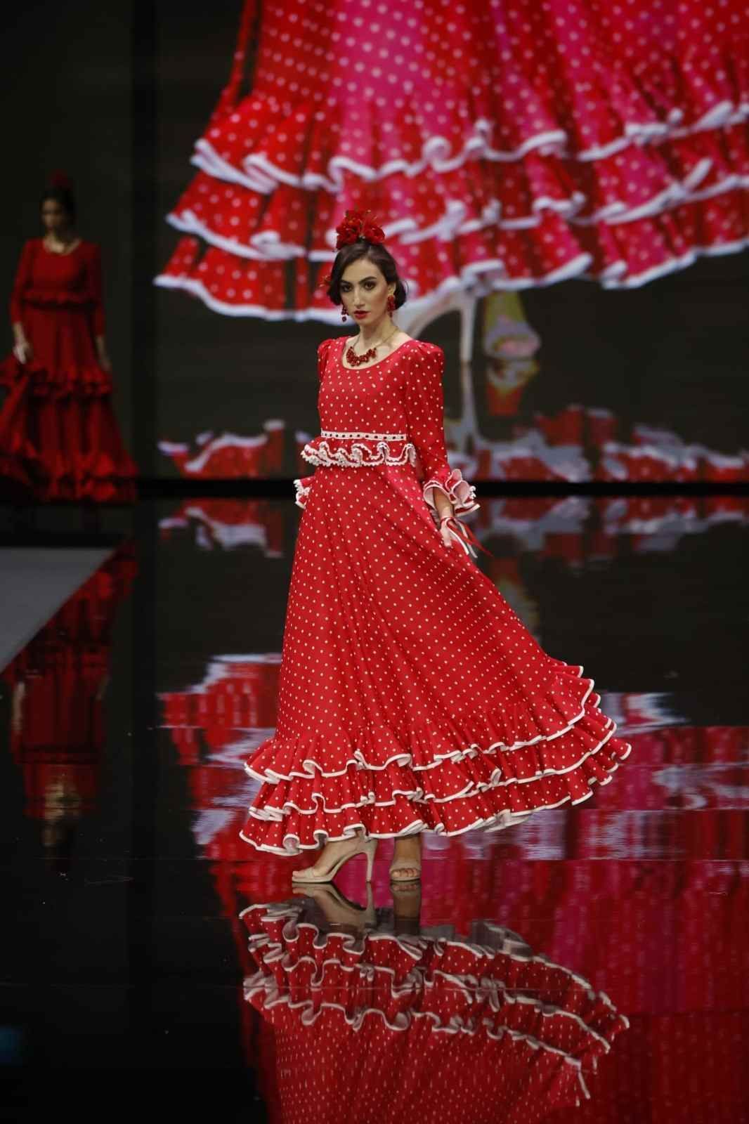 Mujer con un vestido rojo con volantes desfilando por una pasarela con un fondo de reflejo espejado.