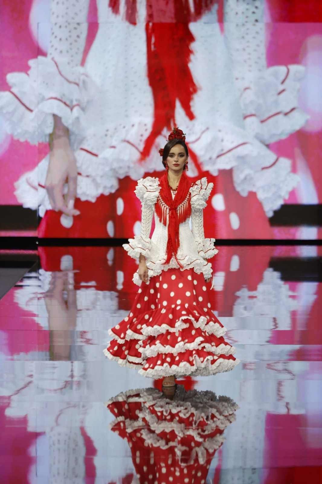 Modelo con un vestido floral rojo y blanco en una pasarela con un fondo rosa y blanco y reflejo.