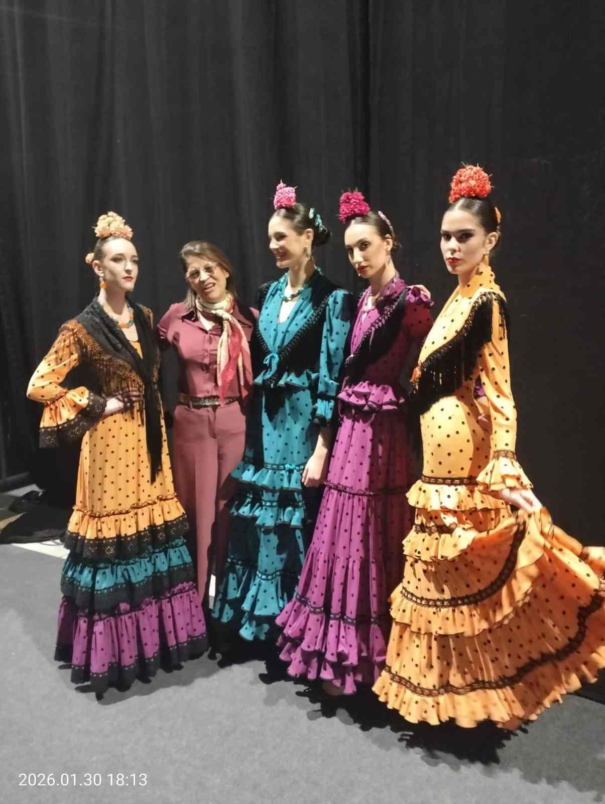 Cinco bailarinas con coloridos trajes de flamenco posan frente a una cortina negra.